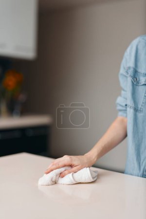 Téléchargez les photos : Nettoyage d'hygiène : Table de cuisine d'essuyage de jeune femme avec la pulvérisation et le tissu sur fond en bois - en image libre de droit