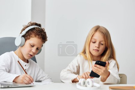 Téléchargez les photos : Heureux enfants caucasiens utilisant des ordinateurs portables pour elearning à la maison Ils sont assis ensemble à une table dans leur salon confortable, portant des écouteurs et se concentrant sur les leçons en ligne - en image libre de droit