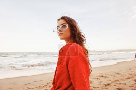 Téléchargez les photos : Femme souriante dans les lunettes de soleil, profiter de la liberté des océans au coucher du soleil : Un portrait coloré dans des vêtements à la mode - en image libre de droit