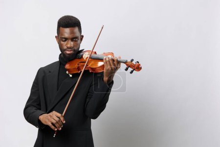 Photo for Elegant African American man in tuxedo playing violin against white background in classical music performance concept - Royalty Free Image