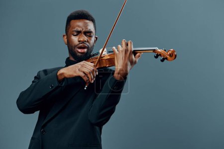 Photo for African American man in a suit playing the violin on a gray background in a graceful and elegant performance - Royalty Free Image