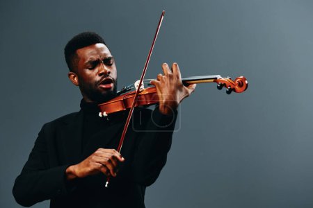 Photo for African American man playing violin in black suit on gray background, artistic music performance concept - Royalty Free Image