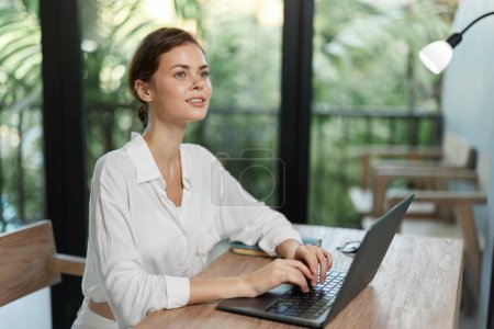 Photo for Happy Freelancer Working from Home with Laptop in a Cozy Interior A smiling woman, dressed in a casual summery outfit, is typing away on her laptop at her home office workspace The modern, stylish - Royalty Free Image