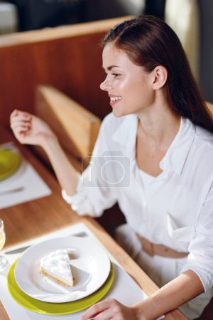 Foto de Mujer feliz disfrutando de una cena romántica en casa, sonriente y extática mientras come, con un entorno de mesa moderno y elegante celebrando una cita especial con un pastel casero y una copa de vino, creando una - Imagen libre de derechos