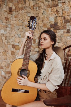Photo for A woman sitting on a chair holding an acoustic guitar in front of a brick wall - Royalty Free Image