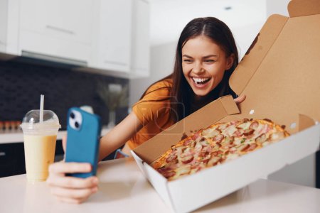 Photo for Woman holding pizza taking selfie with phone and pizza box, enjoying delicious Italian meal and capturing the moment on camera - Royalty Free Image