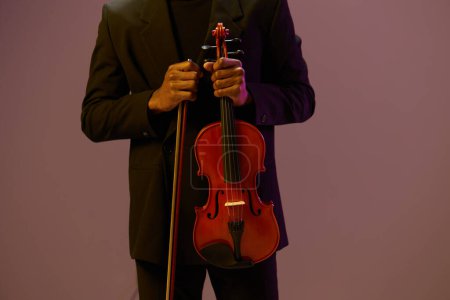Musician in elegant suit playing classical violin in front of vibrant purple stage lights