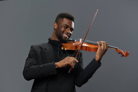 Téléchargez les photos : Jeune homme afro-américain talentueux jouant du violon avec passion sur un fond gris neutre - en image libre de droit