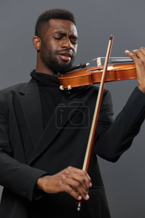 Photo for Elegant African American man in black suit playing violin on gray background in studio setting - Royalty Free Image