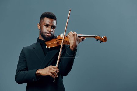 Photo for Talented African American man in a suit playing the violin against a neutral gray background - Royalty Free Image