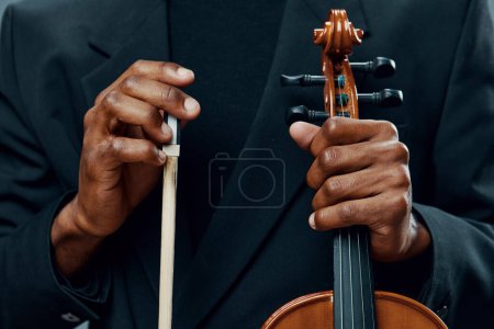 Téléchargez les photos : Gros plan des mains tenant l'arc d'un violon, capturant la touche délicate et l'art de jouer de la musique - en image libre de droit