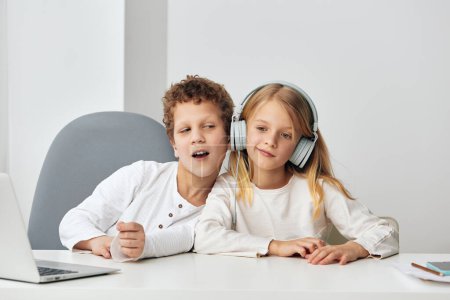 Photo for Happy boy and girl sitting at home in the living room, engrossed in their online elearning session They are using laptops, headphones, and tablets, fully immersed in their studies The room is filled - Royalty Free Image