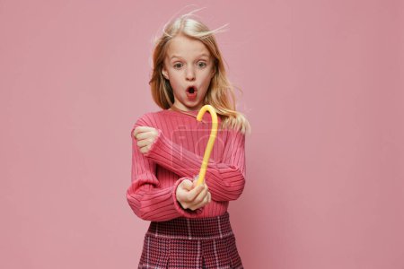 Téléchargez les photos : Écolière heureuse avec sucette rose, Joie expressive et surprise sur fond de studio élégant - en image libre de droit