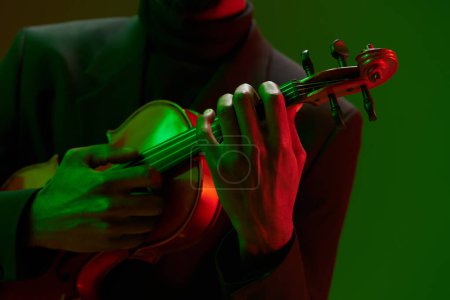 Téléchargez les photos : Gros plan vibrant de l'homme jouant du violon avec la lumière verte et rouge fond éclairant - en image libre de droit