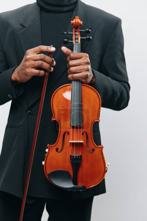 Foto de Elegante hombre afroamericano en traje negro sosteniendo un violín sobre un fondo blanco - Imagen libre de derechos