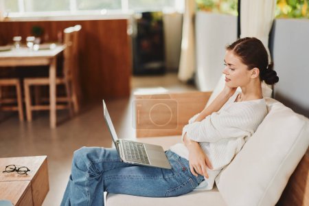 Téléchargez les photos : Week-end détendu femme bénéficiant d'achats en ligne sur ordinateur portable dans le salon confortable - en image libre de droit