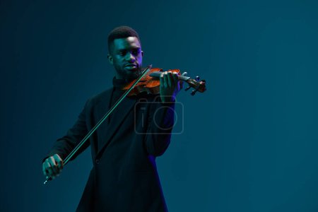 Téléchargez les photos : Afro-Américain portant un costume noir jouant du violon sur un fond bleu vif - en image libre de droit