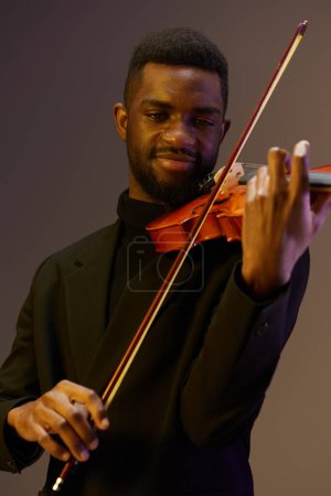 Classiquement habillé homme tenant violon souriant sur fond noir dans élégant portrait tourné