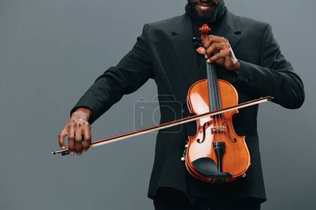 Téléchargez les photos : Élégant homme afro-américain en smoking jouant du violon sur fond gris avec grâce et talent - en image libre de droit
