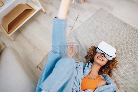 Foto de Diversión de realidad virtual: una mujer sonriente disfrutando de una experiencia de juego futurista en casa con gafas VR en el sofá - Imagen libre de derechos