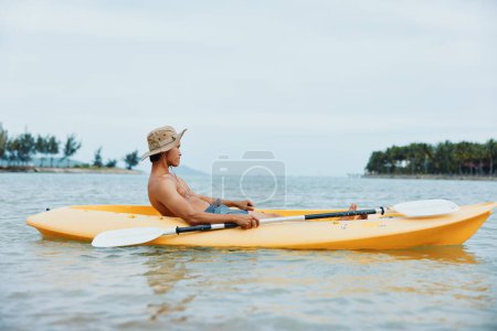 Foto de Aventura en kayak soleado: Hombre remando un kayak en una playa tropical. - Imagen libre de derechos