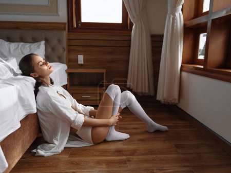 Foto de Mujer sexy joven sentado junto a la cama por la mañana, acogedor en casa en un día libre, ropa interior cómoda, estilo de vida de vacaciones con una sonrisa. Foto de alta calidad - Imagen libre de derechos