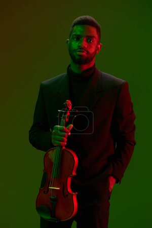 Photo for Elegant man in formal attire holding violin in front of vibrant green and red background - Royalty Free Image