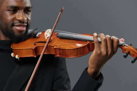 Téléchargez les photos : Afro-Américain en costume noir jouant du violon sur fond gris, créant une atmosphère musicale animée - en image libre de droit