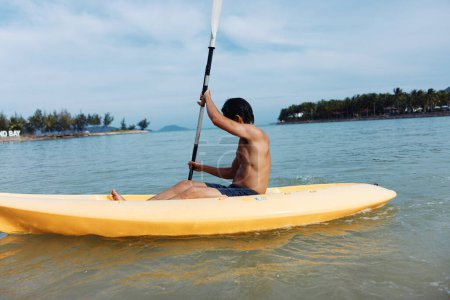 Glückliche asiatische Mann Kajak fahren auf einem tropischen Strand