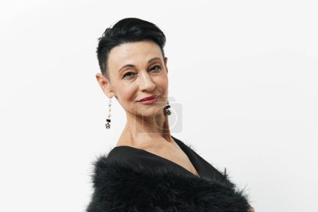 Photo for Elegant woman with short hair in black dress and fur coat standing in front of white wall - Royalty Free Image