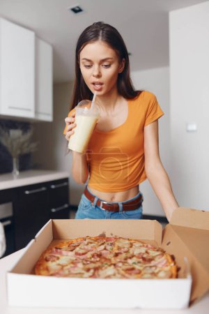 Photo for Woman standing in front of pizza box holding glass of milk in hand, making a food choice - Royalty Free Image