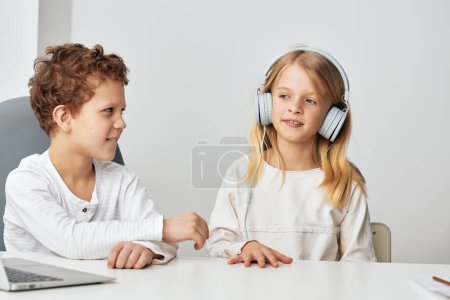 Photo for Child studying at home using a laptop and headphones for online education, accompanied by a boy They are happily engaged in elearning, sitting at a table in the living room The background shows a cozy - Royalty Free Image