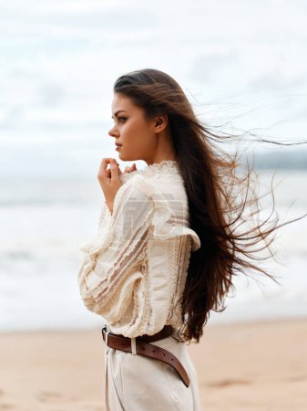 Foto de Felicidad de verano: Una hermosa joven disfrutando de la relajación y la libertad en una playa, con el viento soplando a través de su romántico cabello rubio, frente al océano azul - Imagen libre de derechos