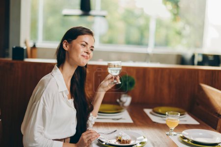 Photo for Romantic Dinner Date Smiling Woman Enjoying a Homemade Meal with Wine In this stylish dining room, a beautiful brunette woman sits at a trendy table, surrounded by a warm and inviting ambiance She - Royalty Free Image