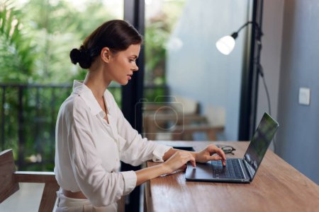 Photo for Smiling Woman Working from Home on her Laptop in a Cozy Indoors Workplace with a Summery Bali Vibes - Royalty Free Image