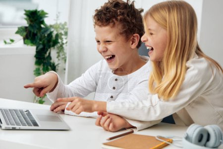 Téléchargez les photos : Enfants heureux étudiant en ligne à la maison en utilisant des ordinateurs portables dans un salon confortable - en image libre de droit