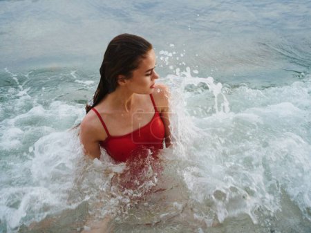 Téléchargez les photos : Femme couchée sur l'océan sur la plage dans les vagues dans un maillot de bain rouge, des vacances à l'hôtel. Photo de haute qualité - en image libre de droit