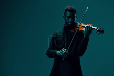 Téléchargez les photos : Elégant musicien en costume noir performant avec violon sur fond bleu vif - en image libre de droit