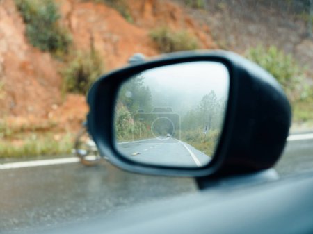 Photo for Journey Through the Raindrop-streaked Mirror: A Fast-paced Road Trip Adventure on the Wet Green Countryside Highway - Royalty Free Image