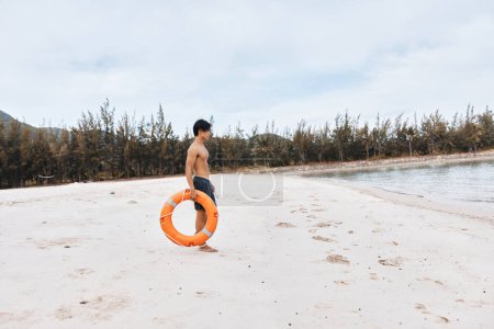 Téléchargez les photos : Gardien de la mer : un sauveteur asiatique vigilant assurant la sécurité et le sauvetage sur une plage d'été animée - en image libre de droit