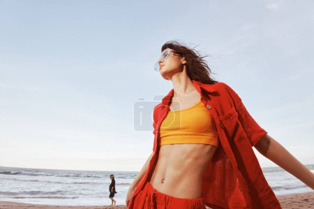 Téléchargez les photos : Femme souriante sur la plage, embrassant la liberté et la joie, contre le coucher de soleil coloré sur l'océan - en image libre de droit