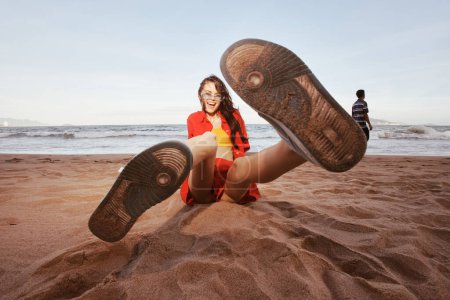 Téléchargez les photos : Mode plage insouciante : Femme souriante en tenue tendance, se détendre sur le sable en grand angle portrait d'été - en image libre de droit