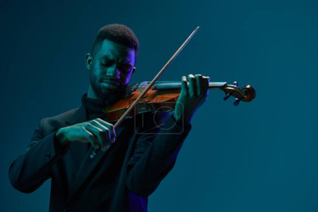 Téléchargez les photos : Elégant musicien en costume noir se produisant sur violon sur un fond bleu vif - en image libre de droit