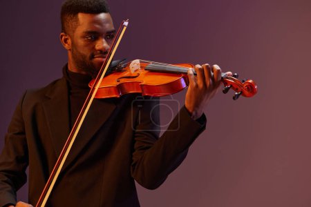 Téléchargez les photos : Élégant homme afro-américain en costume noir jouant du violon sur fond violet vibrant - en image libre de droit