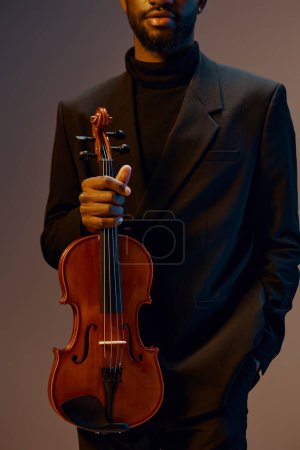 Téléchargez les photos : Élégant homme afro-américain en smoking jouant du violon devant lui sur fond gris - en image libre de droit