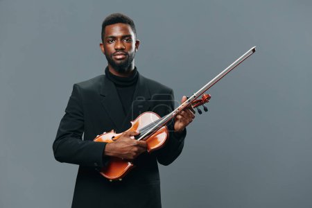 Photo for Professional African American man in suit holding violin against gray background in studio setting - Royalty Free Image