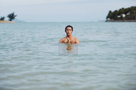 Téléchargez les photos : Plaisir de nager dans le paradis tropical : l'homme asiatique profite de vacances à la plage, éclaboussures dans l'eau bleue de l'océan - en image libre de droit