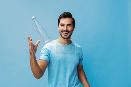 Téléchargez les photos : Main homme bleu attrayant isolé mode de vie de l'eau fond t-shirt heureux studio portrait boisson bouteille boire joyeux sain sport frais sourire - en image libre de droit