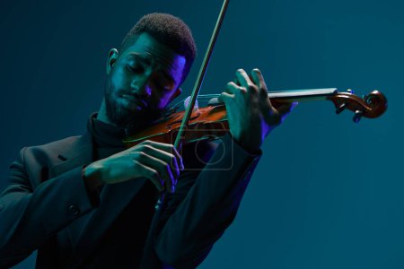 Foto de Elegante músico masculino de traje negro tocando el violín sobre un vibrante fondo azul - Imagen libre de derechos
