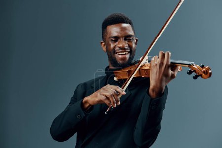 Eleganter Musiker im schwarzen Anzug spielt Geige vor minimalistischem grauen Hintergrund